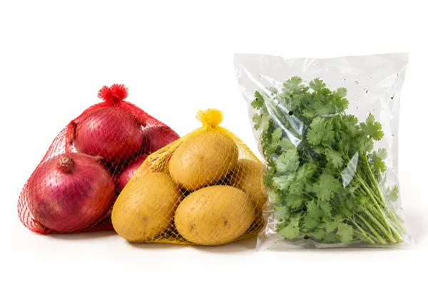 Onions in a red mesh net, potatoes in a yellow mesh net, and coriander in a clear perforated bag